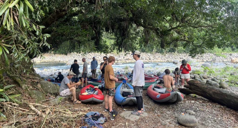 a group of people and several watercraft gather on the bank of a rushing river